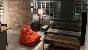A modern living room with a brick wall, a grey sofa, an orange bean bag, and a wooden coffee table.