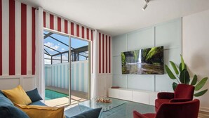 Una sala de estar moderna con una mesa de centro de vidrio, sofás rojos y azules, un televisor de pantalla plana montado en la pared y una puerta corrediza de vidrio que da a un espacio al aire libre.