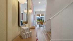 Un pasillo con piso de madera, un espejo grande y una zona de comedor con sillas y una mesa.