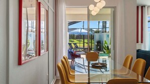 Un comedor moderno con una mesa de vidrio, sillas amarillas y vistas a un patio con mobiliario exterior.