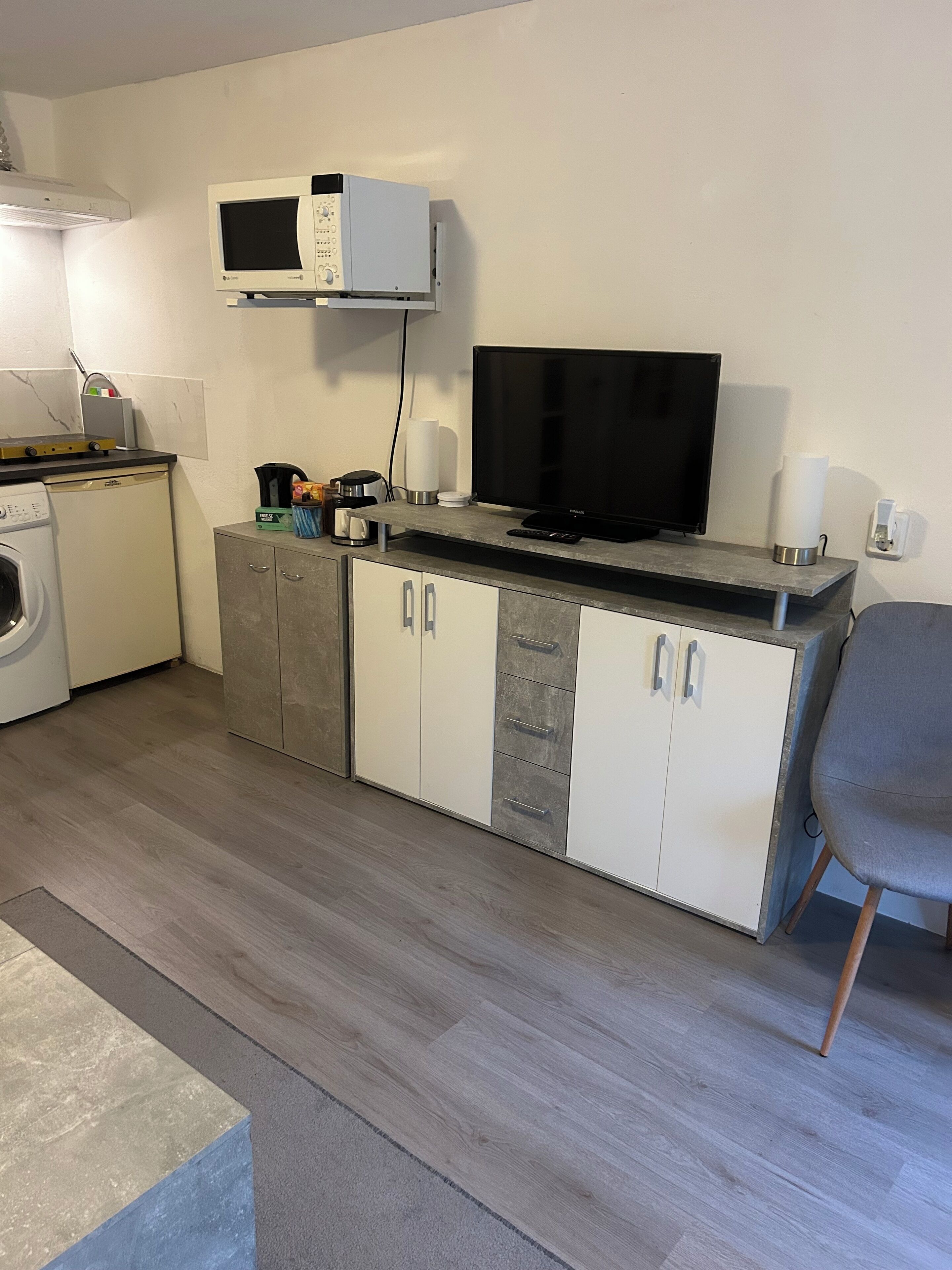 Una cocina compacta con microondas, televisor negro y lavadora.
