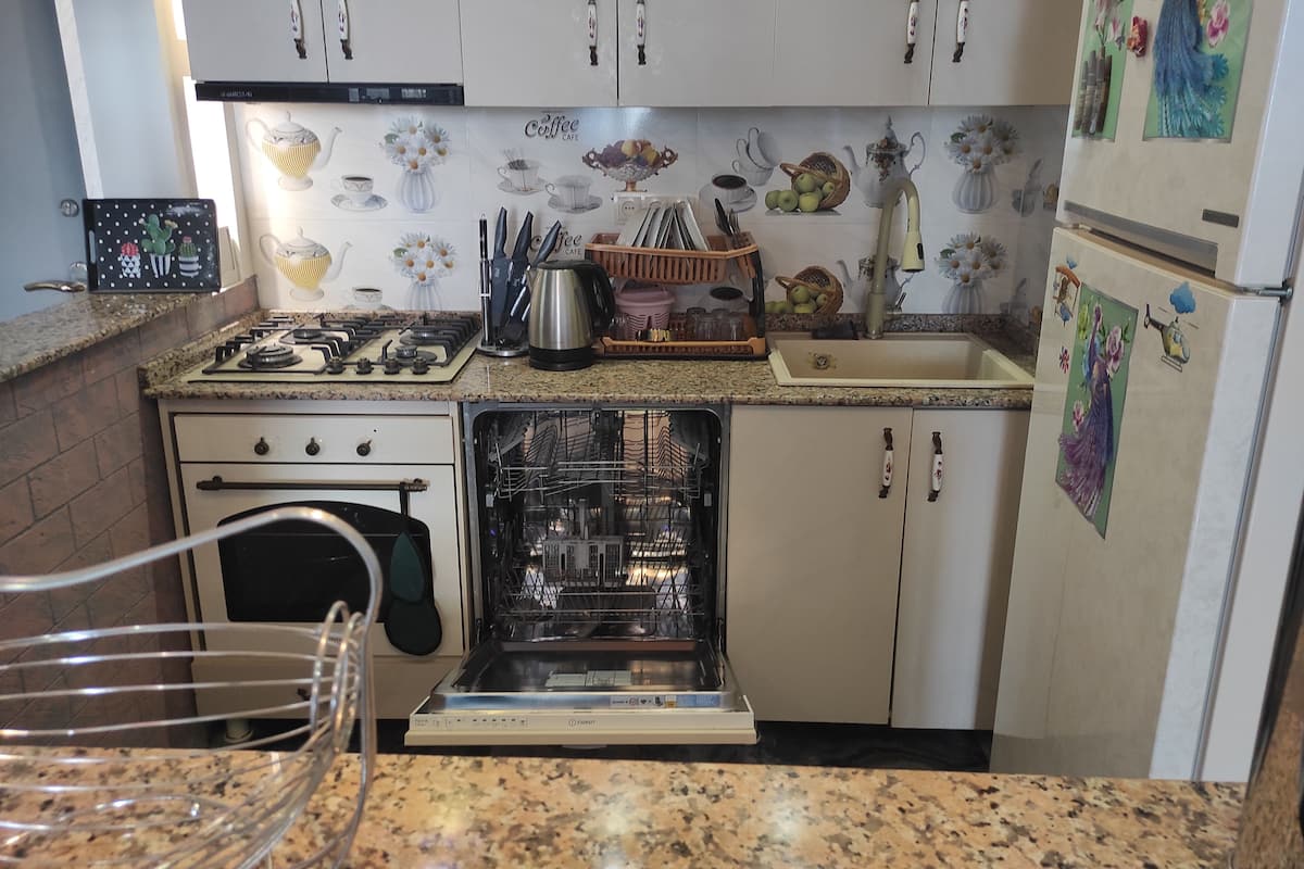 Una cocina con alacenas blancas, estufa, horno, lavavajillas y pileta.