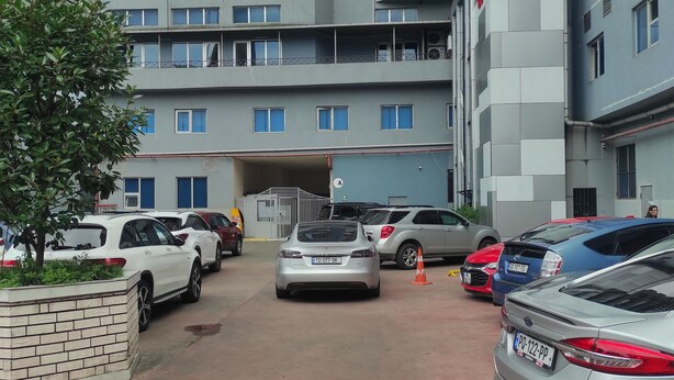 A parking area with multiple cars, a building with balconies, and a tree. - zura (Batumi)