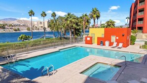 Une piscine avec une eau d’un bleu limpide, un bâtiment aux couleurs rouge et jaune, et des palmiers.