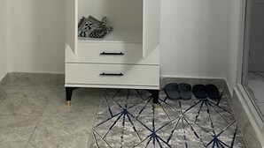 Un armario blanco con dos puertas, un estante pequeño y un par de zapatos en el suelo.