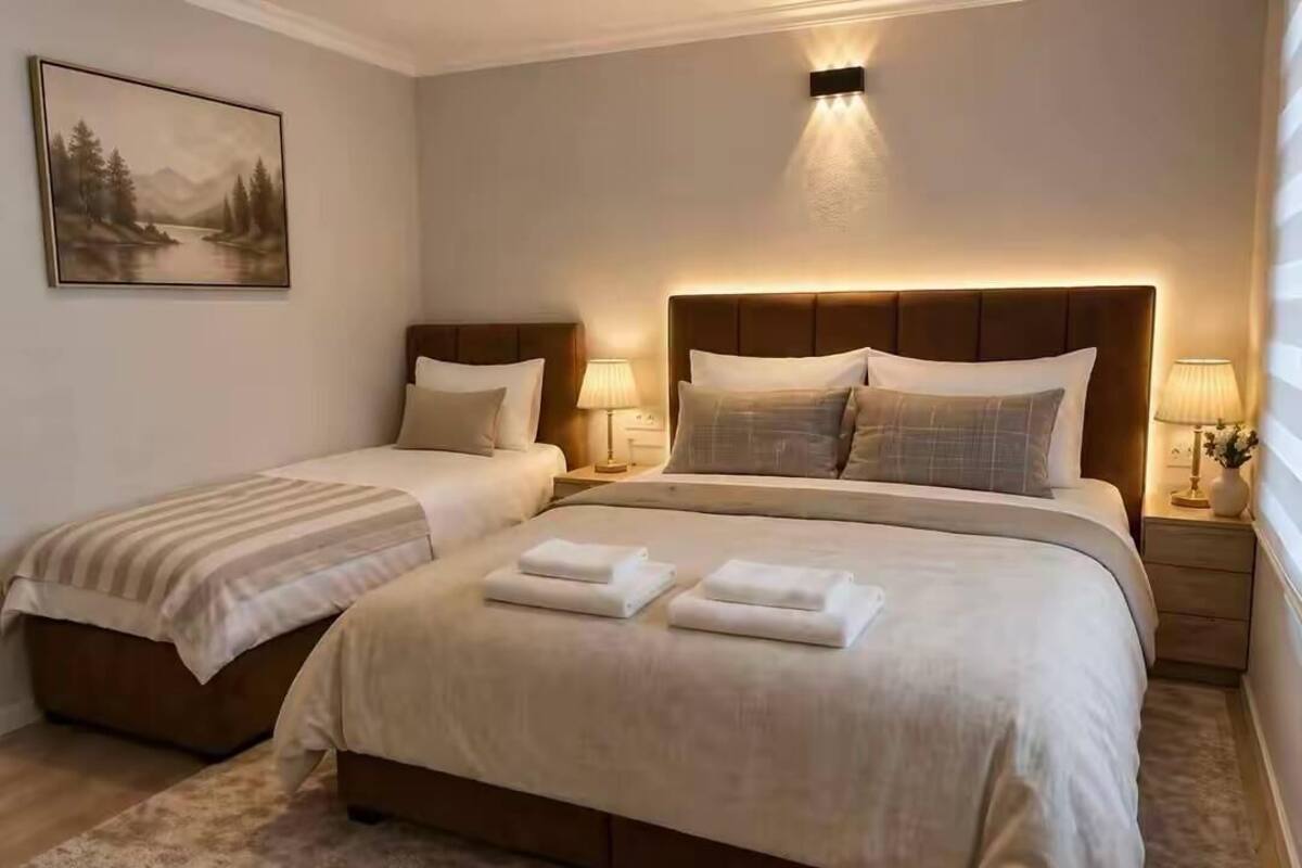 Habitación de hotel con dos camas, un cuadro en la pared y una mesita de noche con lámpara.