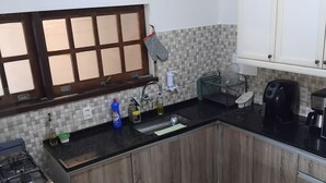 A modern kitchen with wooden cabinets, a black countertop, a built-in stove, and a window with blinds. - Cozy home, your beach house! (Capão Armação dos Búzios)