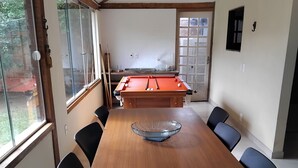 Un comedor con mesa de madera, sillas negras y una mesa de billar al fondo.