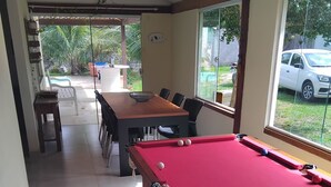 Una mesa de billar en una sala con comedor y ventanas amplias.