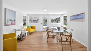 A bright, open-plan living area with a glass dining table, yellow chairs, and a yellow sofa.