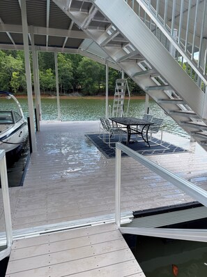 Een overdekte steiger met een boot, een tafel en stoelen, met uitzicht op een rustig wateroppervlak.