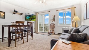 A living room with a sofa, a coffee table, and a dining area with chairs and a table. There is a sliding glass door leading to an outdoor area with a view of the sky and clouds. - 372 Mountain Lodge Ski/Bike/Hike In & Out (Snowshoe)