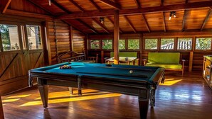 Una mesa de billar en una sala de madera con ventanas amplias y una escalera.