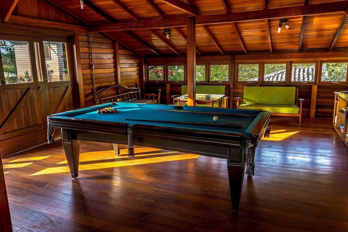 Une table de billard dans une pièce en bois, dotée de grandes fenêtres et d’un escalier.