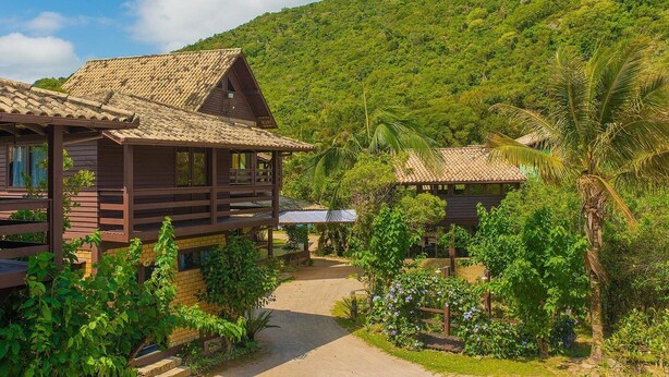 Una cabaña de madera con techo de tejas, rodeada de vegetación exuberante y un paisaje montañoso.