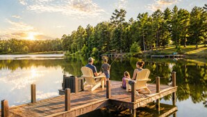 A wooden dock extending over calm water, surrounded by trees and a clear sky.