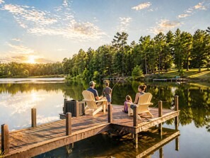 A wooden dock extending over calm water, surrounded by trees and a clear sky.