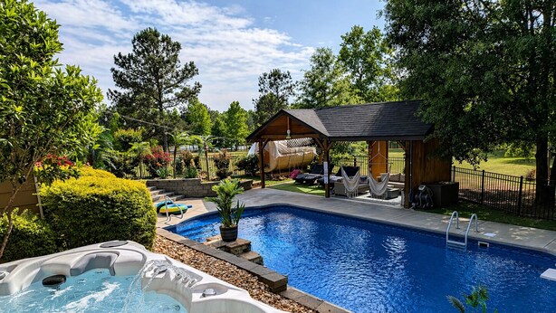 A swimming pool with a hot tub, surrounded by a wooden deck and a gazebo.