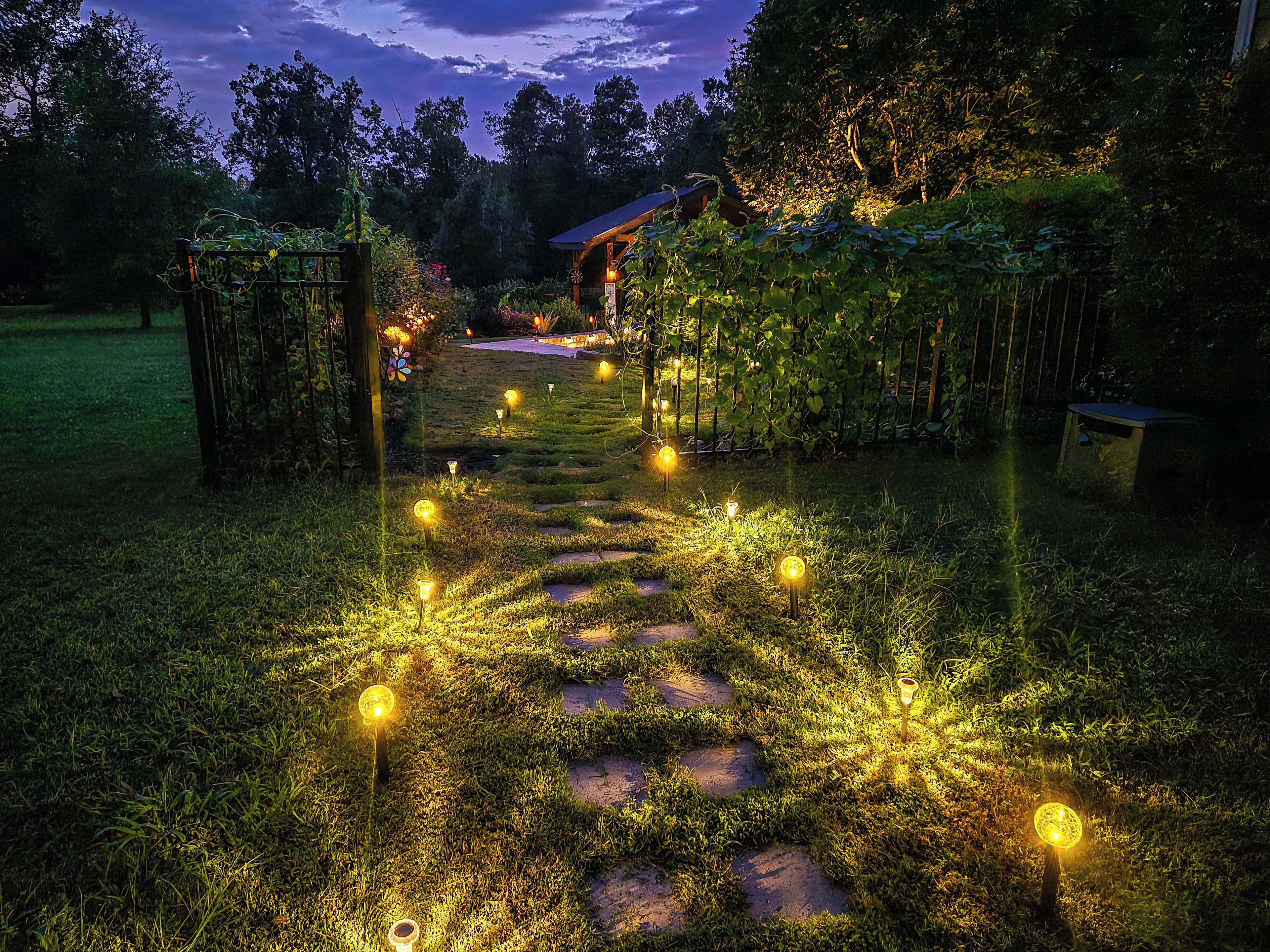 Un sentier de jardin bordé de pierres plates et illuminé par des globes lumineux, qui mène à un bâtiment doté d’un toit rouge.