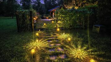 Un sentier de jardin bordé de pierres plates et illuminé par des globes lumineux, qui mène à un bâtiment doté d’un toit rouge.