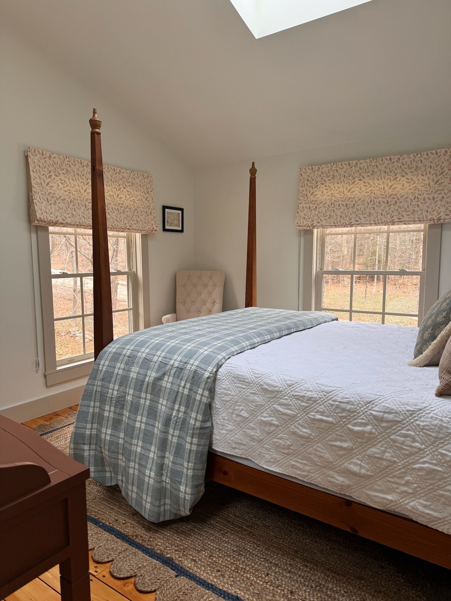 Un dormitorio con una cama grande, una silla y una ventana con vistas a árboles.