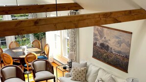 Un salón espacioso con techo alto, vigas de madera, un sofá blanco, una mesa de centro y un comedor con sillas y una mesa.