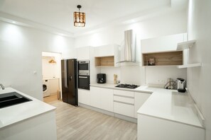 A modern kitchen with white cabinetry, a black refrigerator, a stove, and a hanging light fixture.