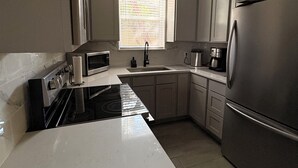 A kitchen with white cabinets, a stainless steel refrigerator, a stove, and a window with blinds. - Cozy Casita in San Antonio Close to sea world- downtown-fiesta Texas-Alamo ranch (San Antonio)