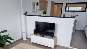 Un salon moderne avec un téléviseur à écran plat posé sur un meuble blanc, une table basse en bois et une plante en pot.