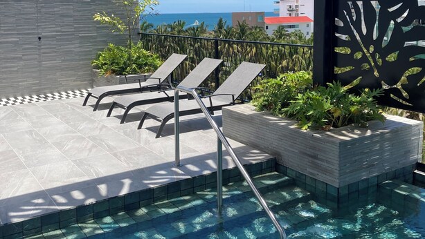 A pool area with lounge chairs, a metal railing, and a view of the ocean.