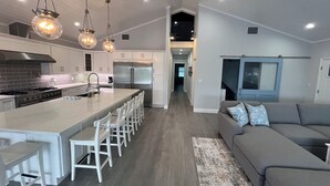A modern kitchen with a central island, white bar stools, and a grey sofa in the living area. - Waterfront, Movie Room, HotTub. 1 house, 2 Options (Tavernier)