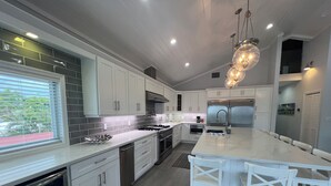 A modern kitchen with white cabinetry, a large island with seating, stainless steel appliances, and a view of greenery outside. - Waterfront, Movie Room, HotTub. 1 house, 2 Options (Tavernier)