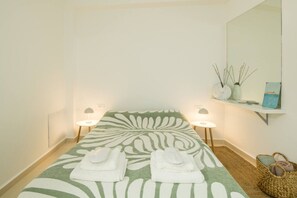 A room with a bed, two bedside lamps, a mirror, a shelf with decorative items, and a woven basket.