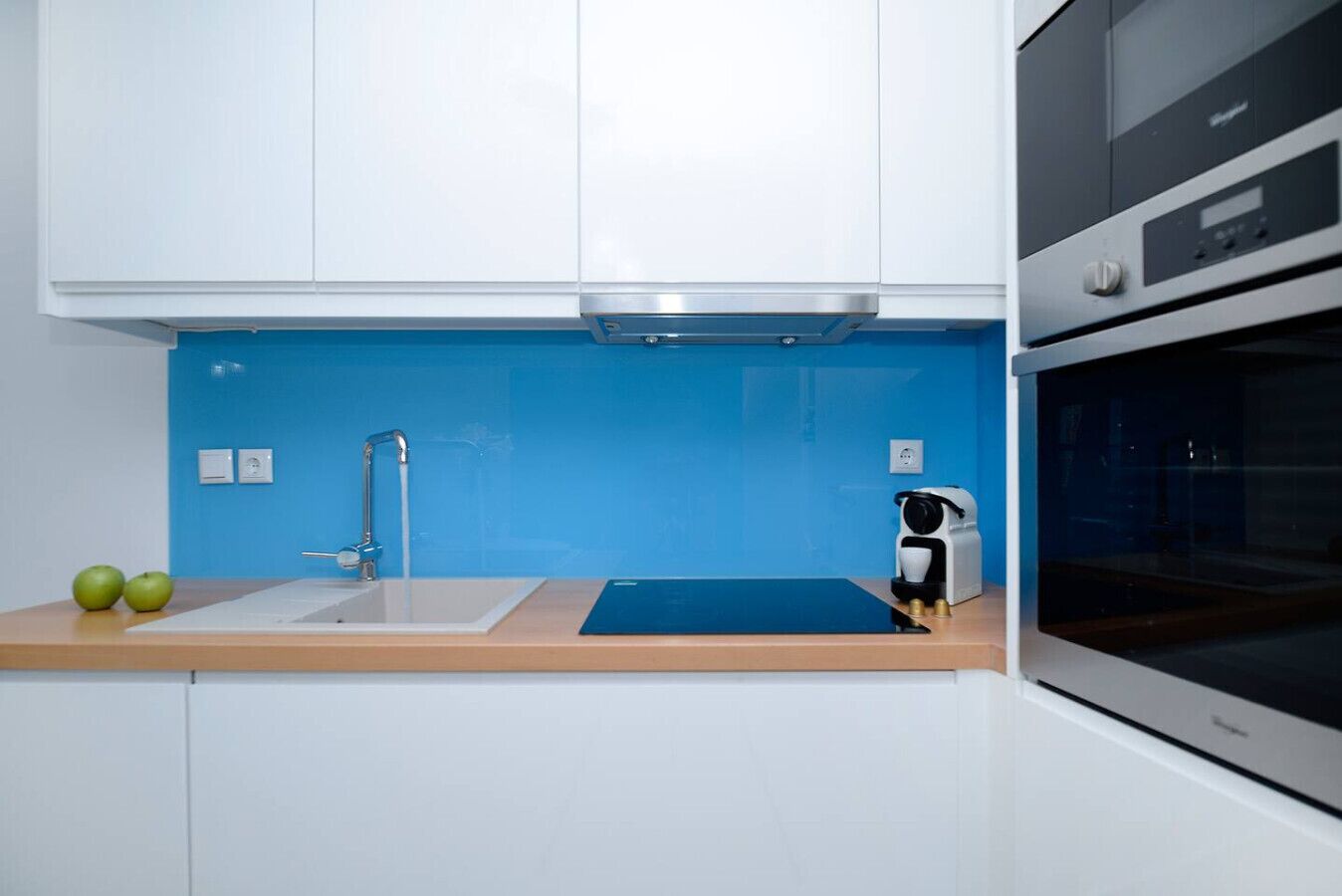 A kitchen with white cabinets, a blue backsplash, a sink, a coffee machine, and an oven.