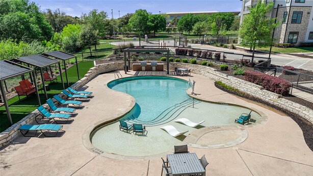 A swimming pool with lounge chairs and a table, surrounded by a landscaped garden and a stone wall.