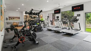 A gym with exercise equipment, a treadmill, and a wall-mounted TV displaying 'NETFLIX'.