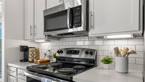 A modern kitchen with stainless steel appliances, white cabinets, and a tiled backsplash.