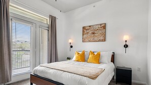 A bedroom with a large bed, two bedside lamps, a wall-mounted artwork, and a window with blinds.