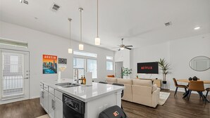 A modern kitchen with a central island, a dining area with a table and chairs, a sofa, and a ceiling fan.