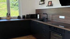 Een moderne keuken met donkere kastjes, een houten aanrechtblad, een ingebouwde oven en een groot raam met uitzicht op groen.
