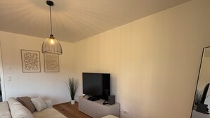 Een moderne woonkamer met een hoekbank, een flatscreen televisie en een hanglamp.