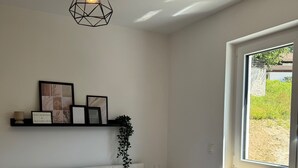 Een slaapkamer met een bed, nachtkastje, raam, wandplank met foto's en een hanglamp.