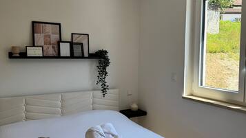 Ein Schlafzimmer mit Bett, Nachttisch, Fenster, einer an der Wand befestigten Ablage mit Bildern und einer Pendelleuchte.