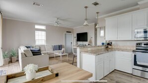 Una cocina moderna con armarios blancos, horno integrado y comedor con mesa y sillas de madera.