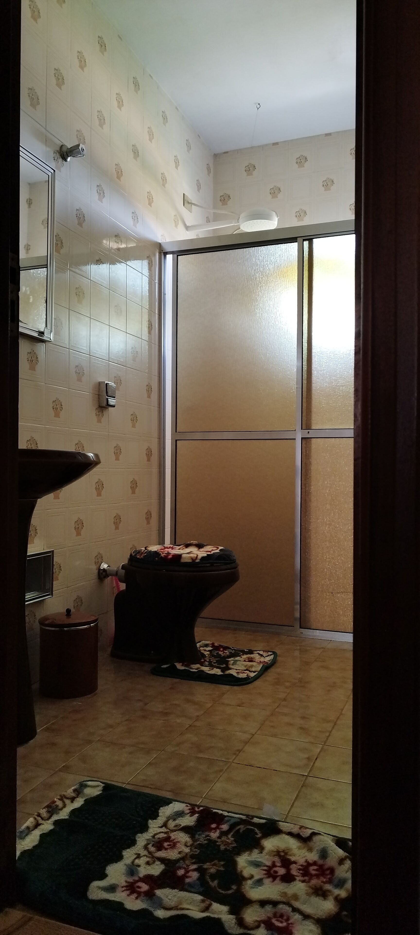 A bathroom with a toilet, a sink, and a mirror. There is a patterned wall and a window with frosted glass.