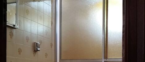 A bathroom with a toilet, a sink, and a mirror. There is a patterned wall and a window with frosted glass.