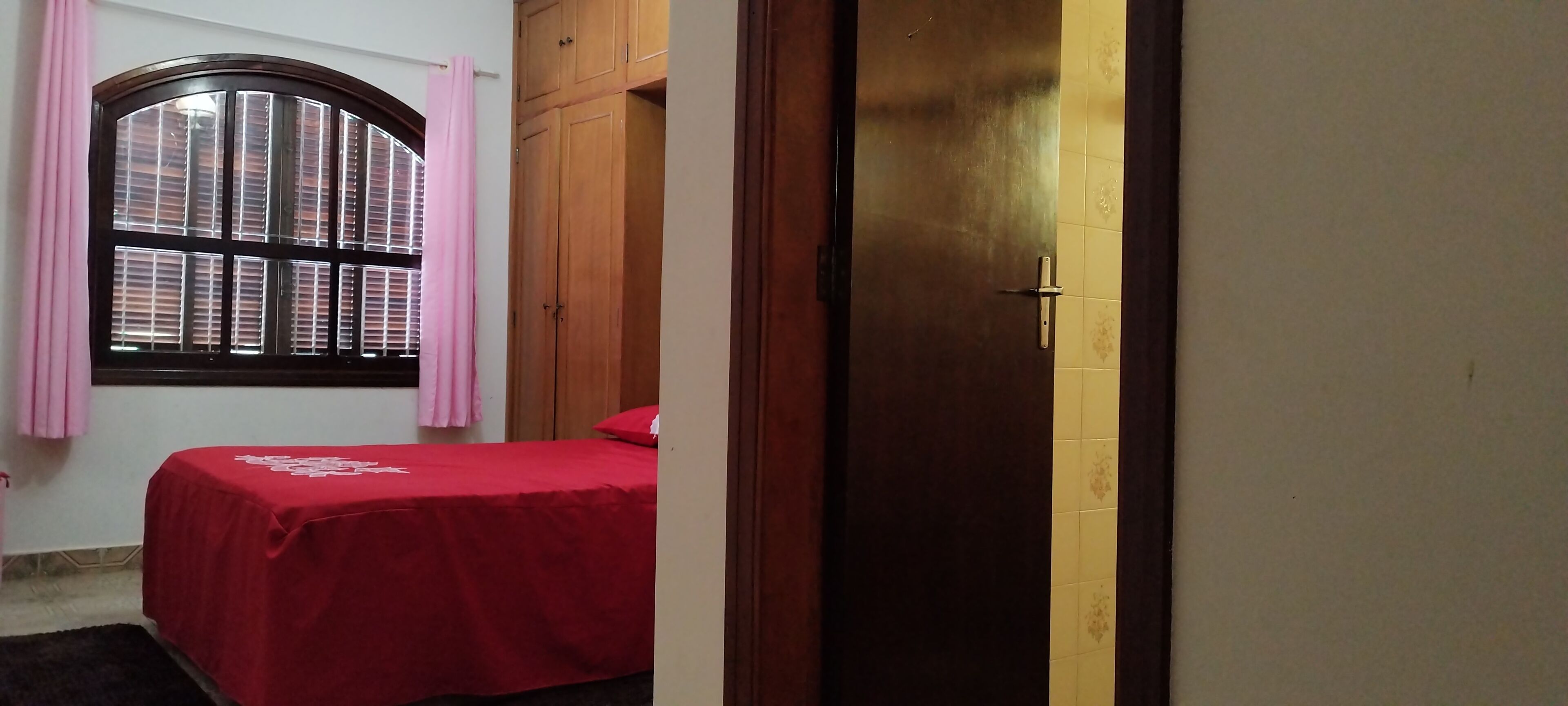 A bedroom with a bed, a wardrobe, a window with blinds, and a door.