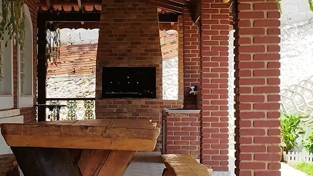 Fachada de ladrillo con un banco de madera, un televisor montado en la pared y una cerca blanca al fondo.