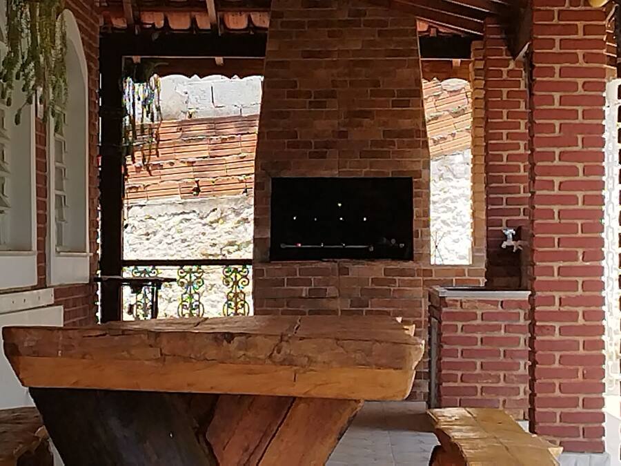 A brick exterior with a wooden bench, a TV mounted on the wall, and a white fence in the background.