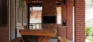 A brick exterior with a wooden bench, a TV mounted on the wall, and a white fence in the background. - Chacara Sorriso 2 (Atibaia)